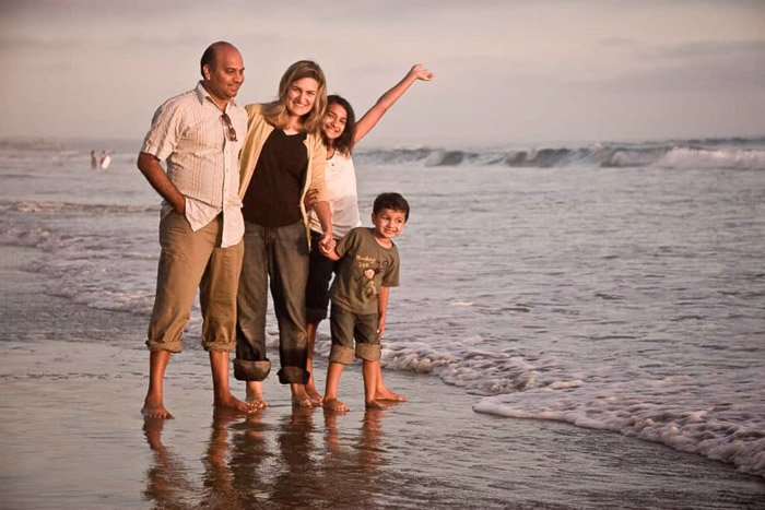 Милая семейная пляжная фотосессия с семьей, гуляющей у берега в одинаковых нарядах