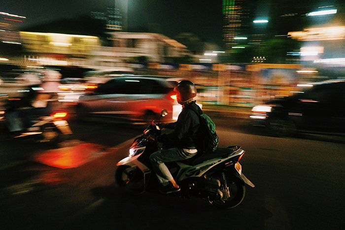 Панорамирование мотоциклиста на размытом фоне движущегося транспорта ночью