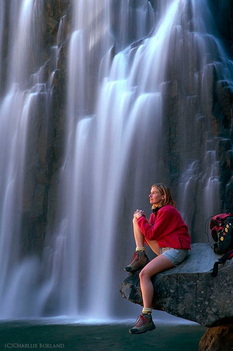 Женщина-фотограф отдыхает на скале у Радужного водопада, Калифорния