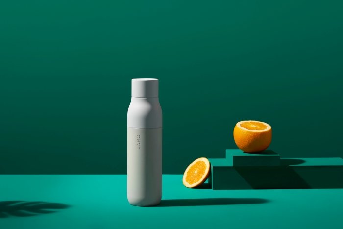 Белая бутылка воды с апельсином на зеленом фоне для фотосъемки товара