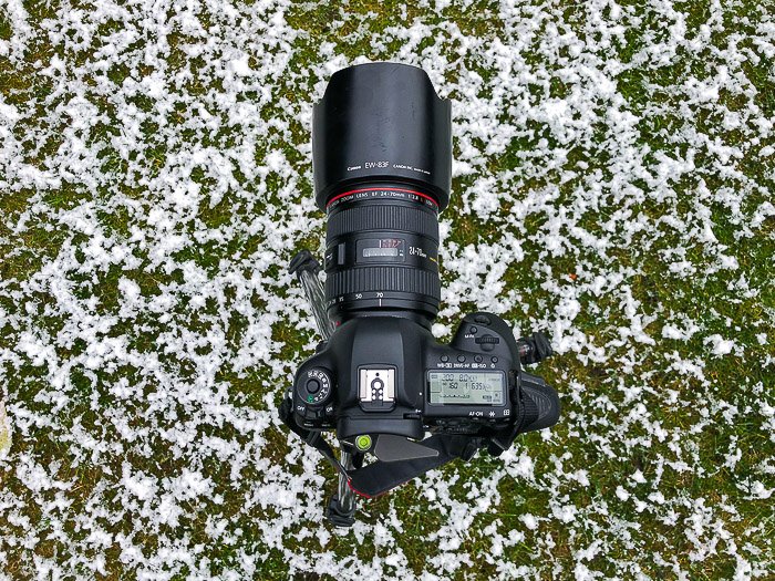 DSLR с зум-объективом лежит на заснеженной траве - оборудование для стоковой фотографии