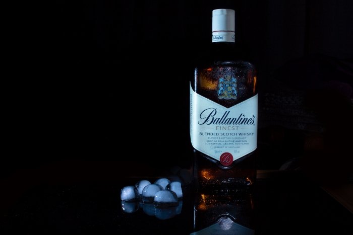 Бутылка виски Ballantines с кубиками льда на черном фоне