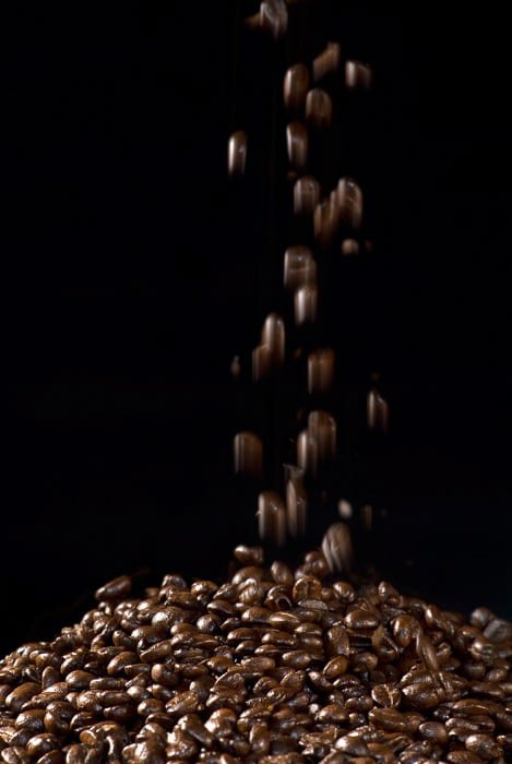 Снимок падающих зерен кофе на черном фоне