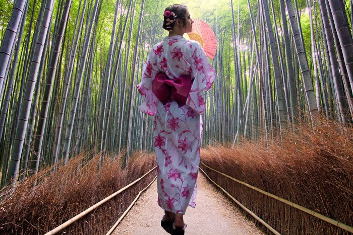 Девушка в традиционном японском платье идет через бамбуковый лес