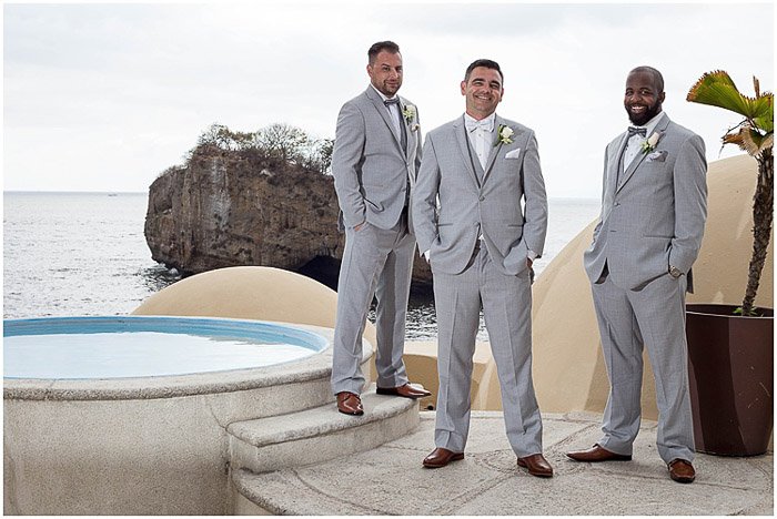 Casual wedding portrait of three groomsmen posing outdoors at a destination wedding 