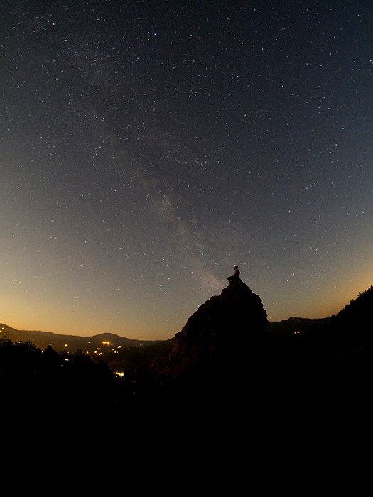 Человек, сидящий на скале под впечатляющим звездным небом