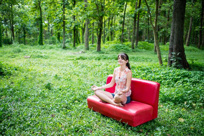 Женщина-модель медитирует на красной кушетке в лесу