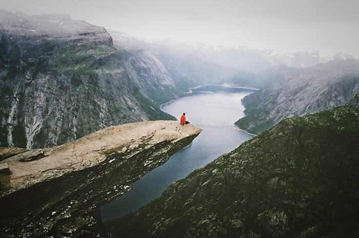 Пример откровенной фотографии человека, сидящего на скале с видом на потрясающий горный пейзаж