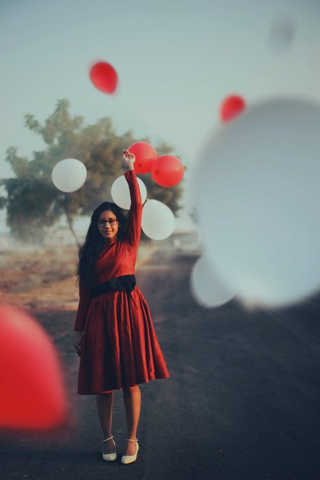 Портрет девушки в красном платье, стоящей среди парящих красных и белых воздушных шаров - идеи для фотобудки