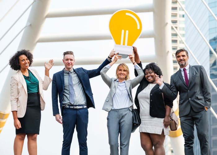 Групповой портрет чрезмерно счастливых сотрудников корпоративного офиса, держащих картонную лампочку - стоковое фото для бизнеса 