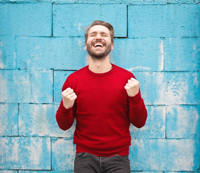 A portrait of an overly happy male model posing against a blue wall - bad stock photos 