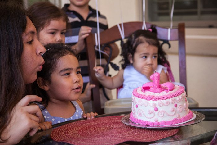 Маленькая девочка задувает свечи на торте на семейном дне рождения - фотосъемка дня рождения