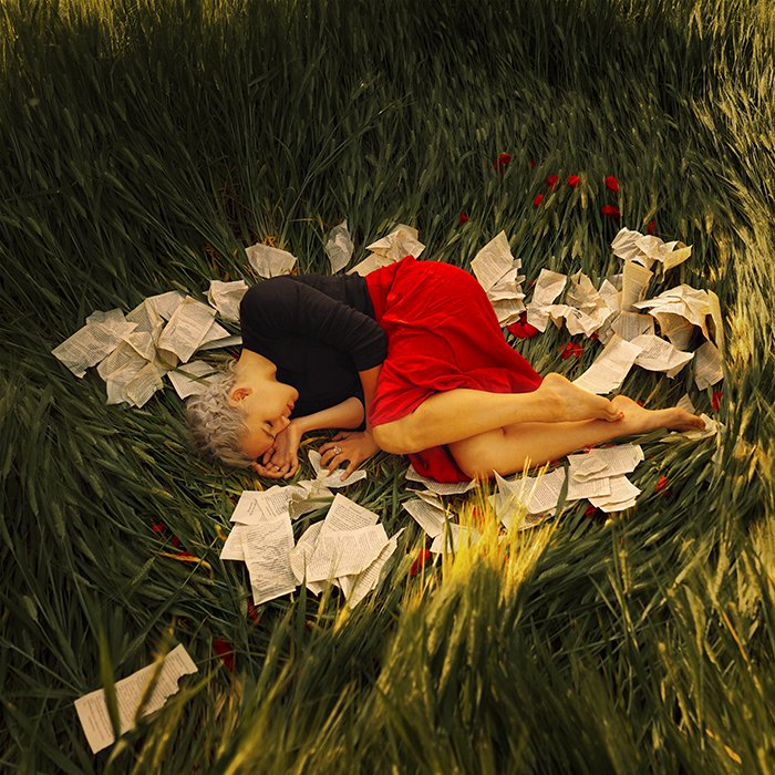 Портрет женской модели, свернувшейся калачиком в траве в окружении бумаги, выполненный Машей Сардари