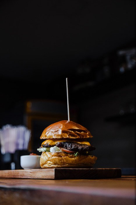 A dark and moody shot of a hamburger on the wooden board - food photography examples