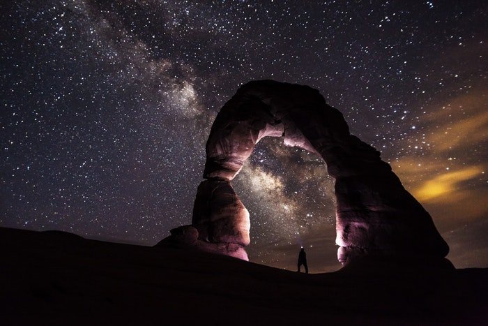Потрясающая ночная фотография с человеком под каменной аркой и звездным небом