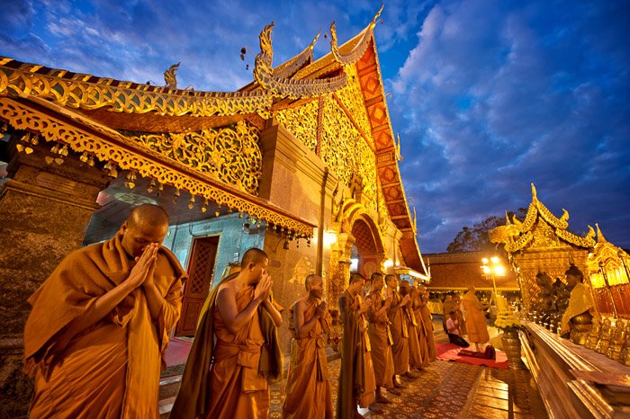 Вереница буддийских монахов, молящихся возле храма в сумерках - малая и большая глубина резкости