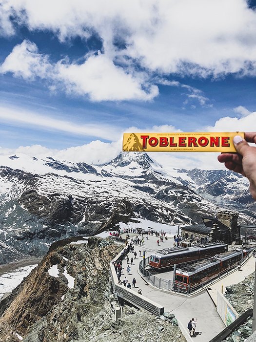 Человек держит шоколадку toblerone на фоне горного пейзажа
