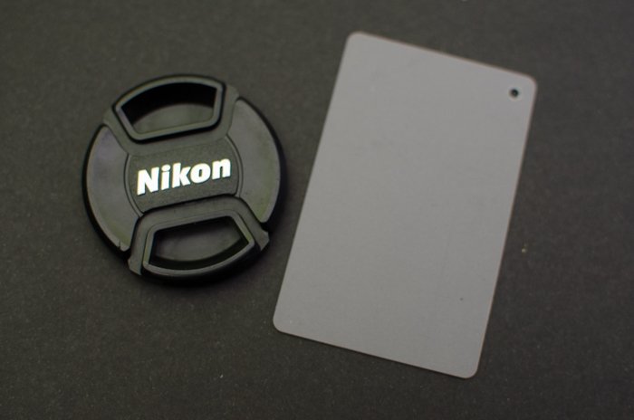 Крышка объектива Nikon на сером фоне с серой фотокарточкой рядом с ней