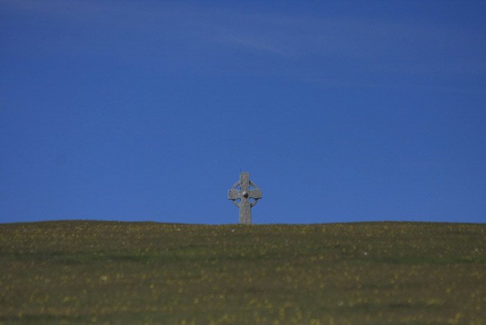 Минималистский пейзажный снимок с каменным крестом под ясным голубым небом