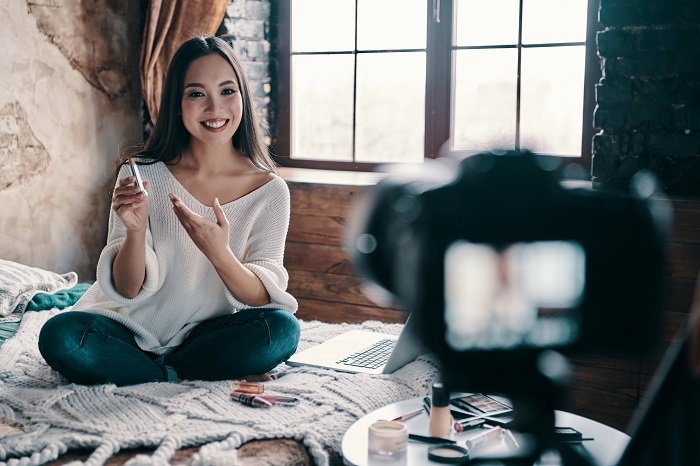 Красивая молодая женщина держит помаду и улыбается во время съемки lifestyle product photography