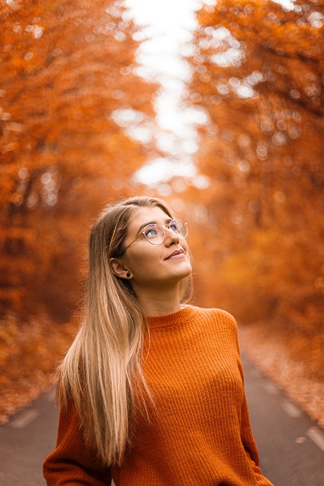Красивая осенняя фотография женщины-модели в оранжевом, позирующей на фоне деревьев с оранжевыми листьями