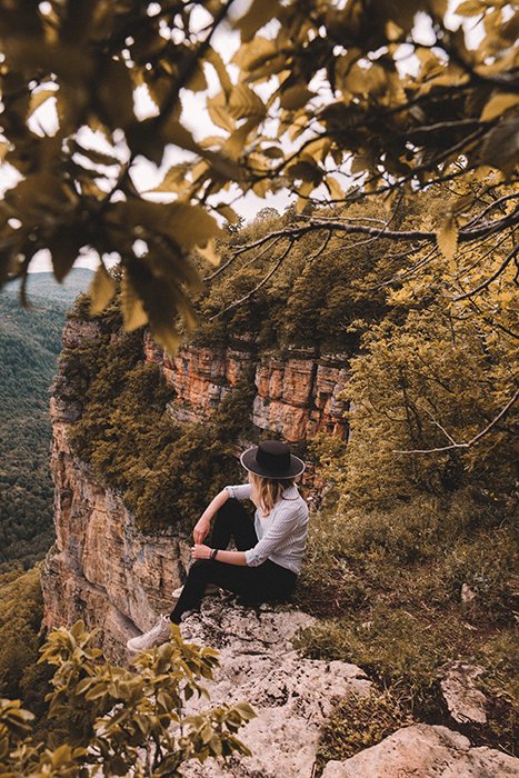 Открытый портрет женщины-модели, сидящей на камнях среди красивого горного осеннего пейзажа.