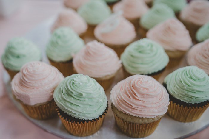 Яркая фотография тарелки розовых и зеленых кексов с глазурью на светлом фоне