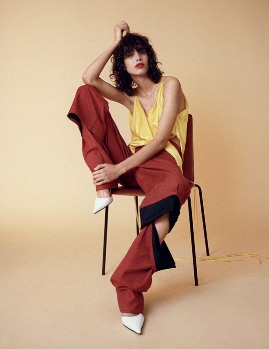 Женщина-модель позирует на стуле на бледно-желтом фоне - модное фото вдохновения