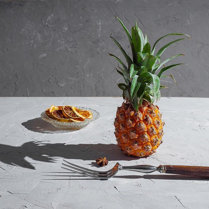 Художественный натюрморт с ананасом и тарелкой апельсинов, снятый со спидлайтом