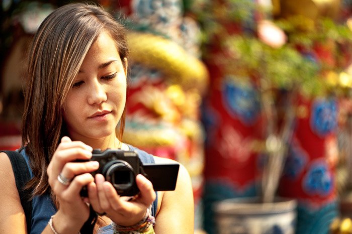Женщина-фотограф держит компактную камеру на размытом фоне - камеры серого рынка