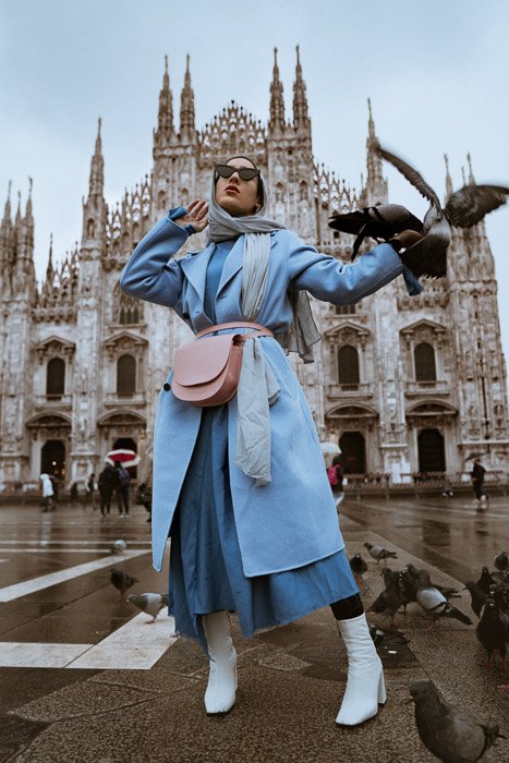 Женщина-модель позирует перед историческим зданием с голубями, летающими вокруг нее - советы по созданию модного лукбука