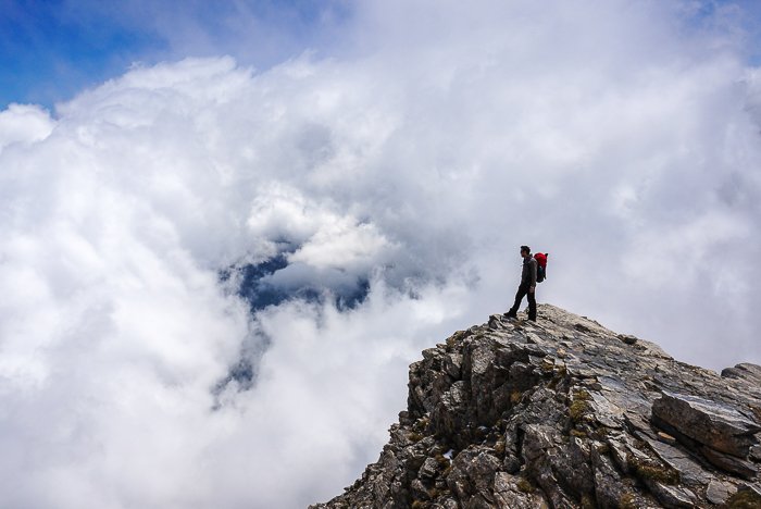 турист, стоящий на скалистой вершине горного ландшафта - навыки приключенческой фотографии