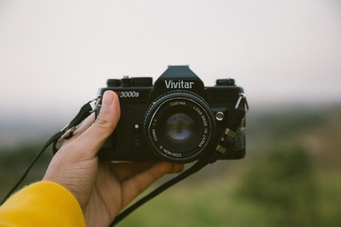 фотограф с вытянутой рукой держит фотоаппарат Vivitar по направлению к снимающему