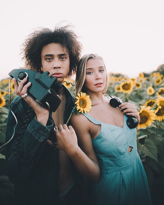минималистичный портрет пары, держащей старомодный телефон в поле подсолнухов
