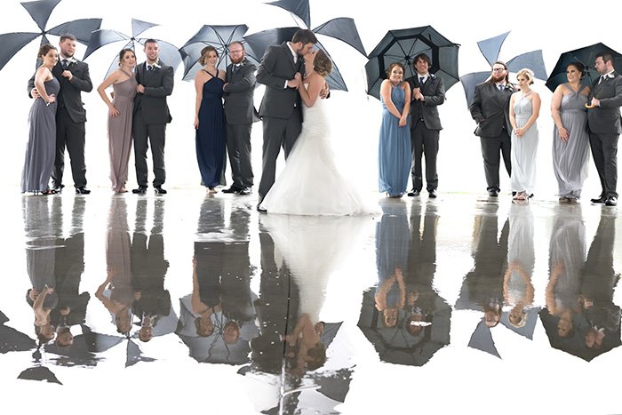 групповой свадебный снимок молодоженов, держащих зонтики под дождем
