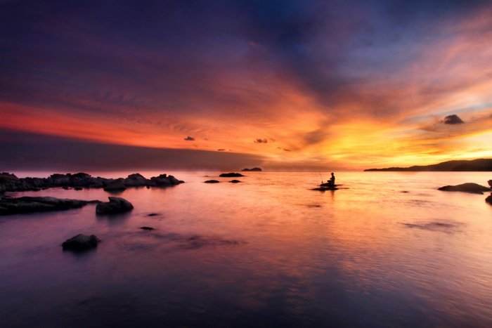 Фотография водного пейзажа с рыбаком на закате в фиолетовых, оранжевых и желтых тонах
