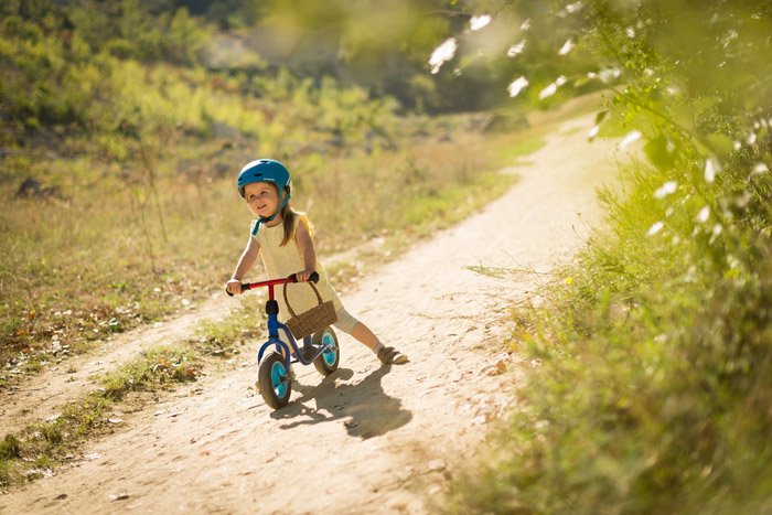Фотография маленькой девочки с маленьким велосипедом на грунтовой дороге