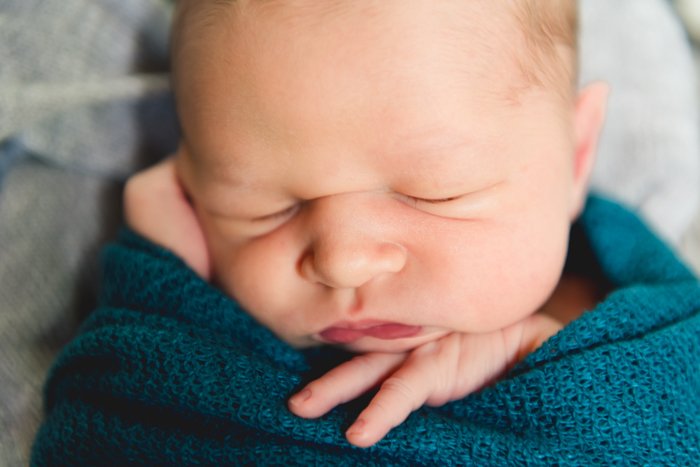 Фотография крупным планом новорожденного ребенка, пеленаемого в бирюзовое одеяло