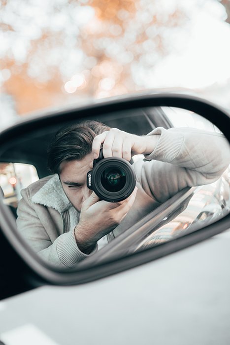 Отражение в зеркале автомобиля, показывающее человека с камерой