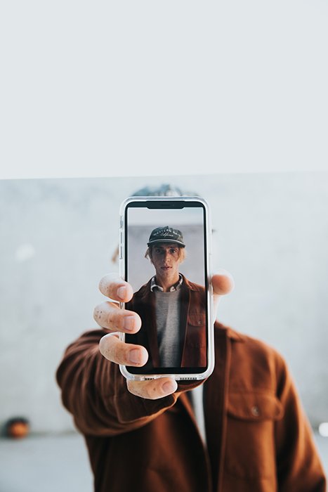 Мужчина держит телефон с камерой и его автопортрет на экране