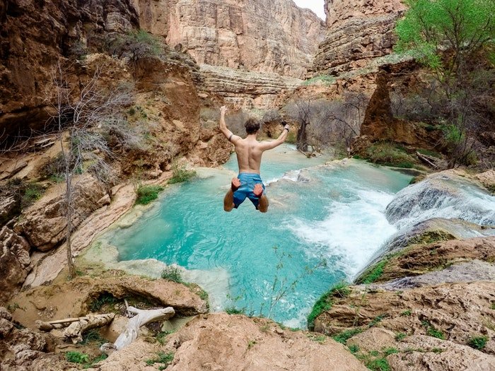 Человек прыгает в бассейн с водой в окружении скалистых гор