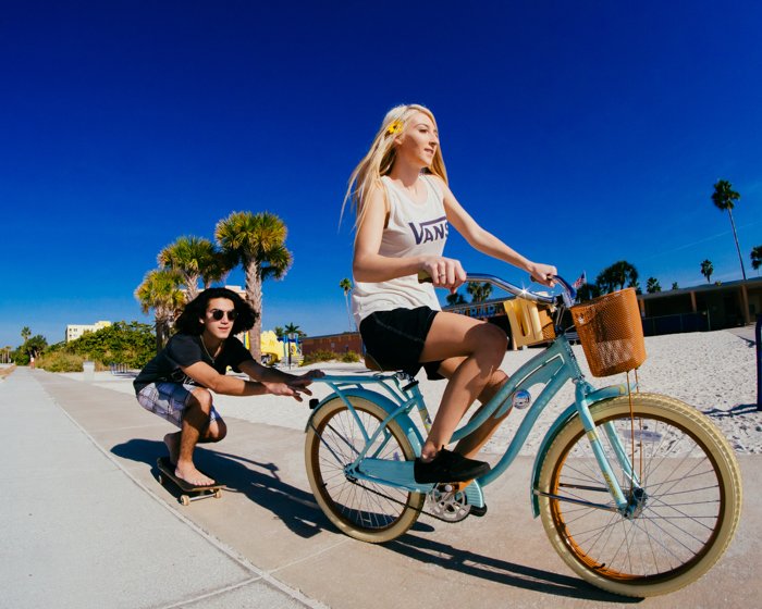 Фотография девушки на велосипеде с парнем на скейтборде, держащимся за велосипед