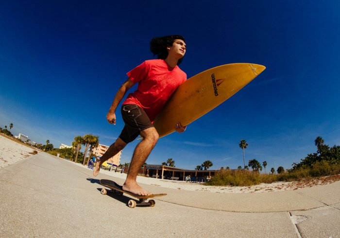 Фотография парня с доской для серфинга в руке на скейтборде