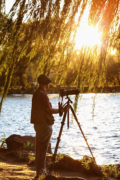 Фотограф настраивает кадр с камерой и штативом у озера