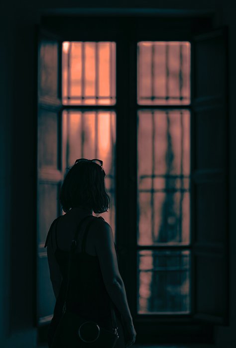 Moody scene of a girl looking out of a window in a dark room