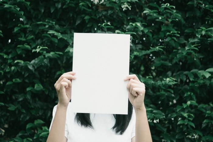 Женщина держит чистый лист бумаги над своим лицом