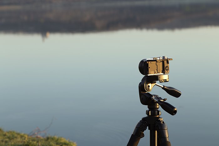 Камера на штативе на фоне озера.