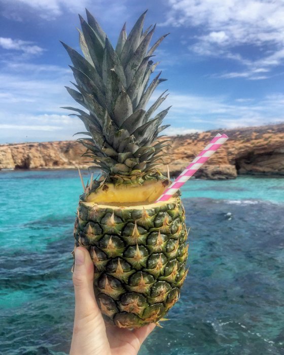 Крутая фуд-фотография для iphone рука держит ананасовый коктейль на фоне морского пейзажа