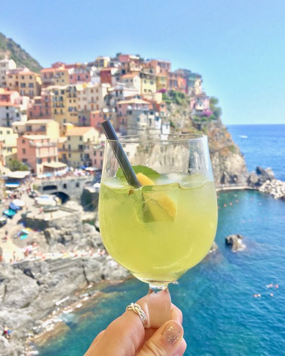 A limoncello spritz held in front of a beautiful coastal town