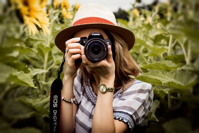 Девушка в поле подсолнухов фотографируется на зеркальную камеру